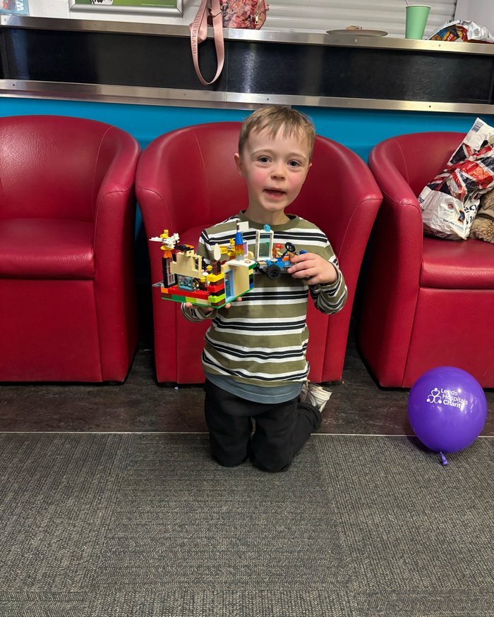 A child proudly holding up a Lego creation, with a Leeds Hospitals Charity balloon nearby