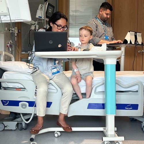Freddie sitting on a hospital bed table between two adults working on laptops
